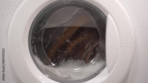 Foamy soap suds churning around shoes in washing machine drum, creating dynamic bubble patterns. Dense white foam envelops footwear during intense cleaning cycle.