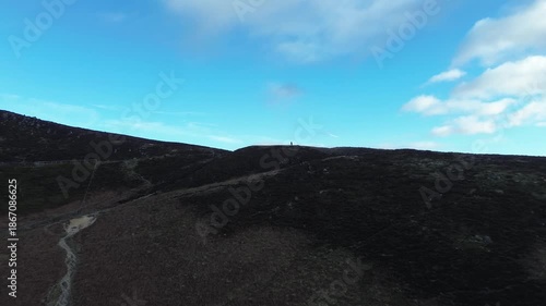A mountain range with a clear blue sky in the background. The sky is dotted with clouds