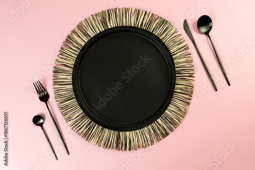 Top view of black wicker table mat, black cutlery on yellow background. Straw round tray, flat lay, copy space. 