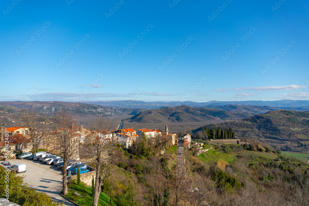 Naklejka premium Wide panoramic view of red tiled rooftops and rolling hills surrounding Motovun, Croatia, under clear daylight at winter 