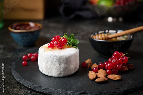 Foto Sliced ​​Camembert dessert cheese on a stone plate with red currants, almond nut and fruit