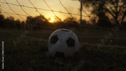 An empty soccer field at sunset with a ball caught in the net, symbolizing the end of the game or beginning of a dream. Ideal for themes of sport, reflection, or hope.