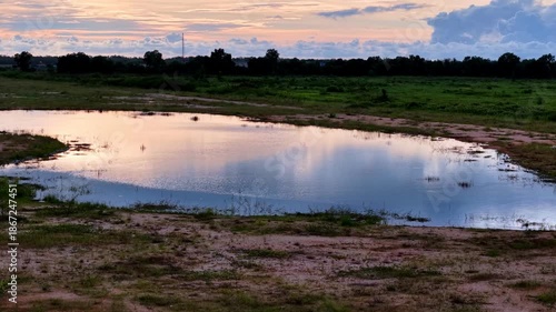 A pond with a reflection of the sky. The sky is orange and pink. The water is still
