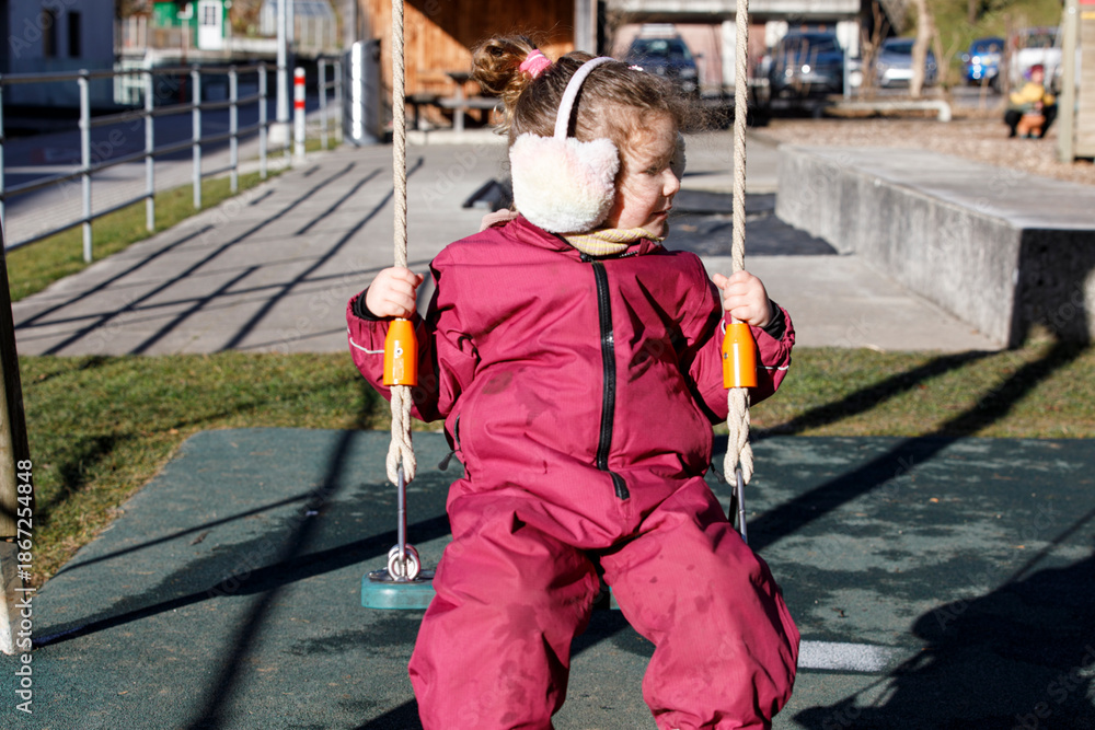 Obraz premium A cute little girl enjoys a day out, wearing warm ear muffs while swinging in the park. Perfect for