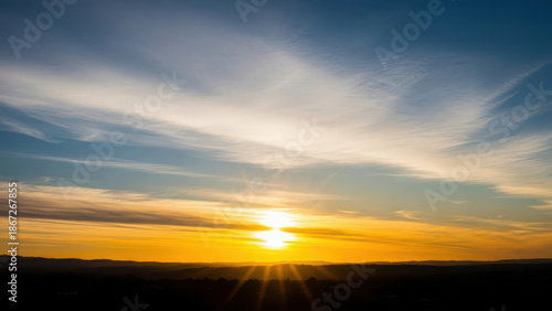 A serene sunrise scene with the sun peeking over the horizon, casting light through scattered clouds.