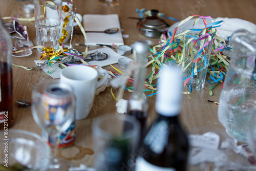 Φωτογραφία Post-party scene with drinks, colorful streamers, and general mess on a wooden table