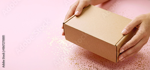 Female hands holding a plain cardboard box on pink background with copy space. Concept of delivery, packaging, online shopping, e-commerce, gift, subscription box, business presentation. 