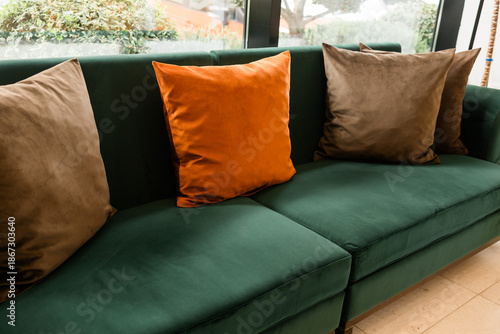 Green velvet sofa with decorative pillows in living room. Comfort, relaxation, and domestic calm expressed through color balance and soft upholstery in modern interior space.