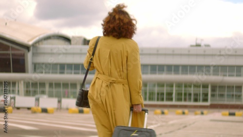 Woman with red hair and yellow coat bring baggage to airport