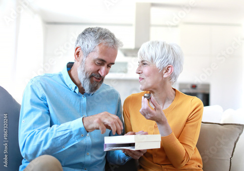 Portrait of a happy senior couple embracing eating chocolate praline from a gift box and having fun at home