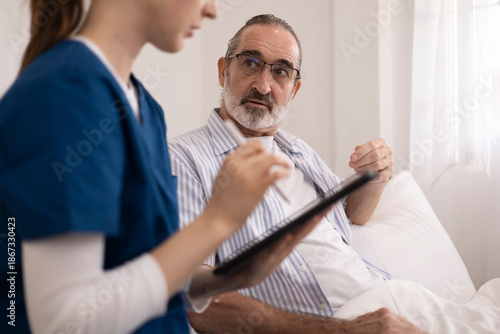 The elderly man is receiving care from a private nurse at home because of his illness. The nurse and patient are using a tablet for bedside consultations to manage their health.