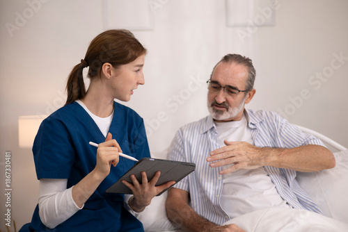 The elderly man is receiving care from a private nurse at home because of his illness. The nurse and patient are using a tablet for bedside consultations to manage their health.