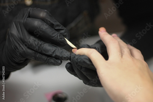 Professional nail technician in black gloves performing precise manicure procedure on client hands