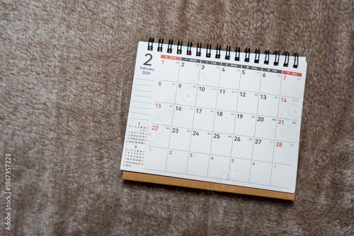 A desk calendar featuring the month of February 2026 displayed prominently on a soft surface. This scene suggests organization and planning for upcoming events.