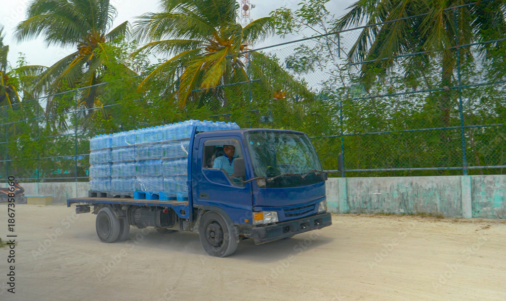Naklejka premium Old lorry delivers pallets full of bottled water to the harbor of exotic island.