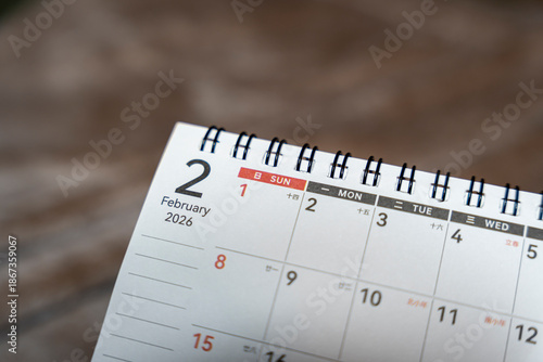 Close-up of a spiral calendar displaying February 2, 2026 with the date highlighted. Pages laid on wood table evoke organization and planning for future events or appointments.