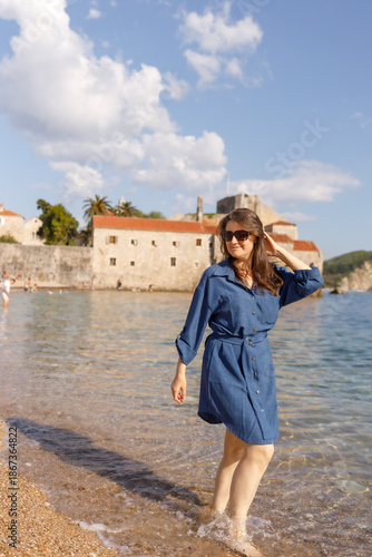 A girl in a short blue dress runs barefoot along the sea shoreline, then stops and spins in place; summer, the Adriatic Sea, vacation