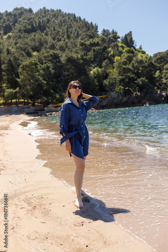 Woman stands barefoot in the water on a sandy beach by the sea on a sunny day