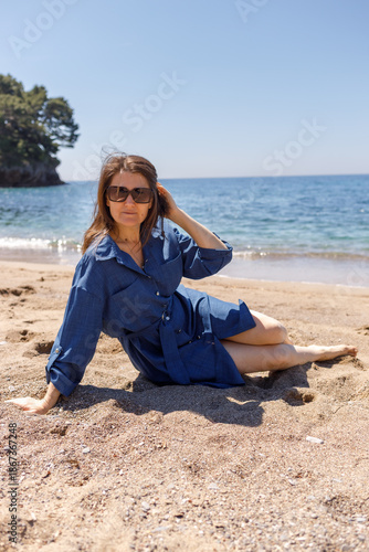 Woman stands barefoot in the water on a sandy beach by the sea on a sunny day
