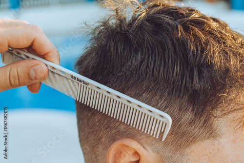A professional barber providing hair cutting and grooming services in a barbershop. This scene represents male grooming, hairstyling, and personal care in a modern or traditional barber environment.