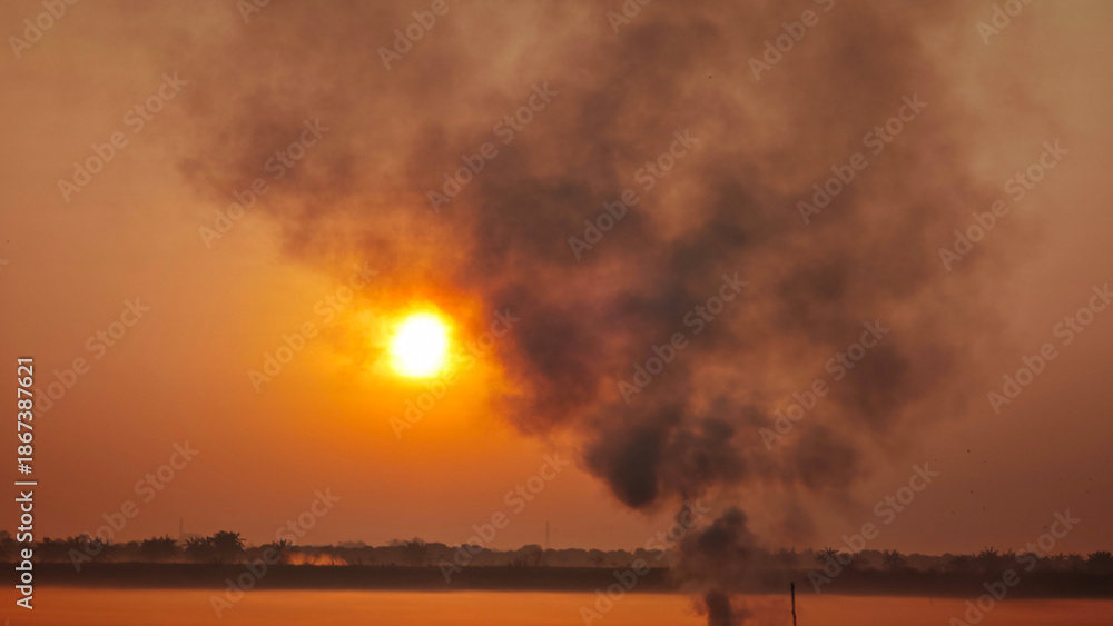 Obraz premium Fires caused by burning agricultural waste such as dry grass and rice straw produce thick smoke, which is a cause of air pollution during sunrise.