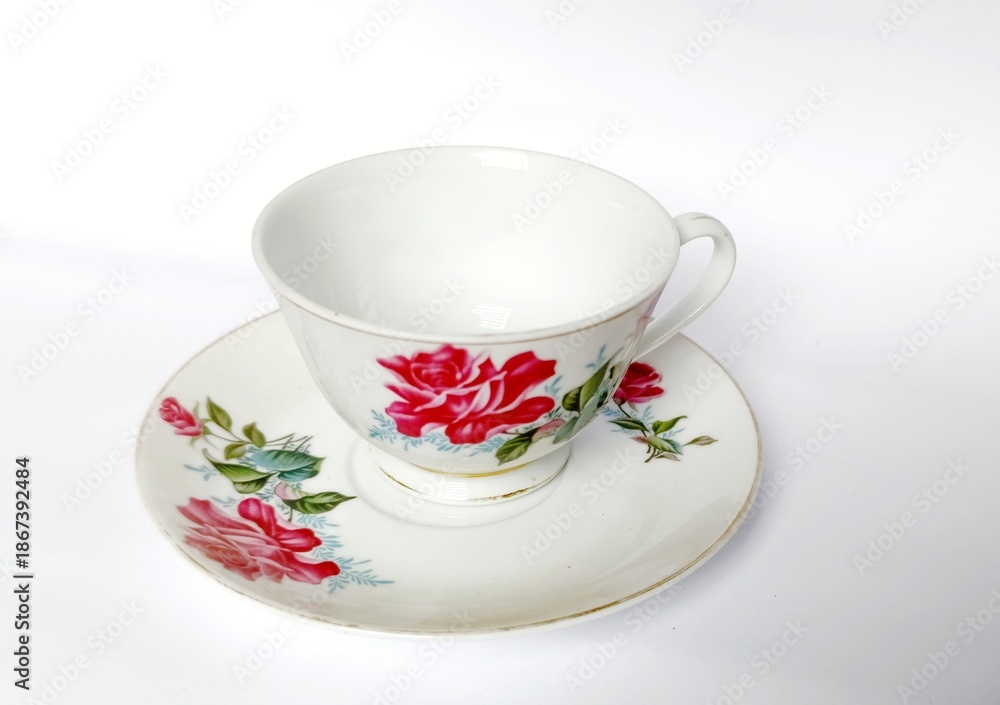 Fototapeta premium White tea cup and saucer with red floral pattern on a plain background.