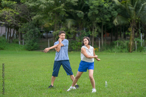 An Asian couple in athletic clothing walking together on a gravel path while holding hands, smiling and enjoying a peaceful moment in the countryside.