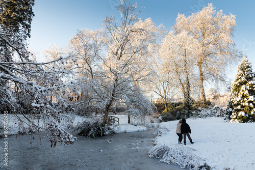 Parc et arbres recouverts de neige avec une mare glacée et personnages emmitouflés, lumière matinale