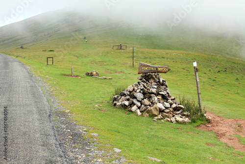 Camino de Santiago sign pointing toward Roncevaux Orreaga mounted on a pile of rocks  and a grave along the mountain route from Saint-Jean-Pied-de-Port, photographed in July 2024.