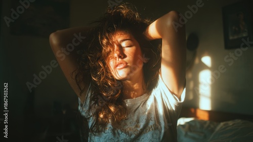 Young woman with wavy brown hair touching her head bathed in warm sunlight creating shadows