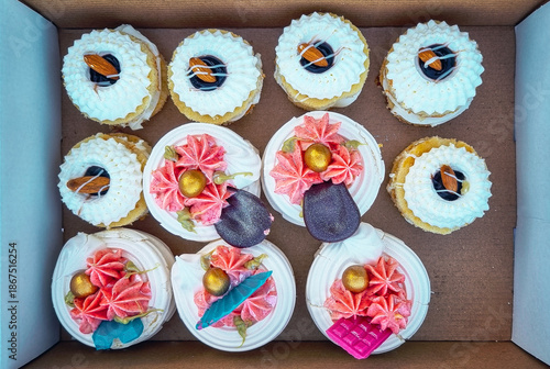 Top view of still life with different types of colorfully decorated cupcakes in a paper box