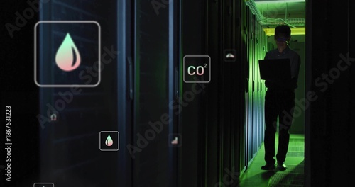 Monitoring Korean tech in long sleeves holding laptop in server aisle, hologram icons, copy space