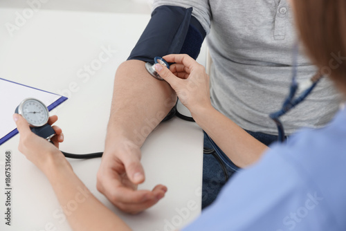Принти на полотні Nurse checking man's blood pressure with sphygmomanometer at table in hospital,
