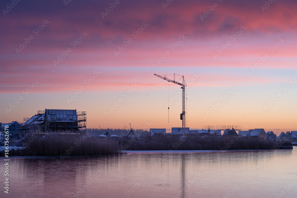 Fototapeta premium A crane at a construction site during a colourful, winter sunrise. Meerstad, the Netherlands.