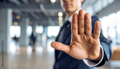 A man in a suit extends his hand with an open palm in a gesture of stopping or refusing. The person shows a clear signal of objection or denial in a professional setting