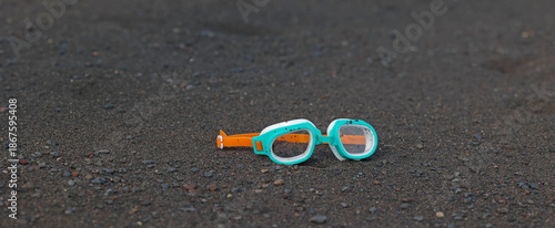 Panoramic close up of turquoise swim goggles resting on black volcanic sand at a Tenerife beach in the Canary Islands, Spain