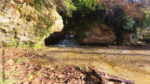 The Golmayo River emerges from a small rock cave at the Fuentetoba natural park, with fallen autumn leaves scattered on the ground, creating a picturesque winter scene in the province of Soria.