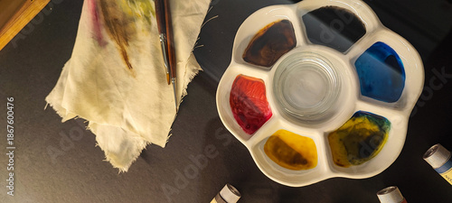 A vibrant watercolor palette, brushes, and stained fabric on a dark background. Concepts of artistic expression, creativity, inspiration, handicrafts, and hobbies.