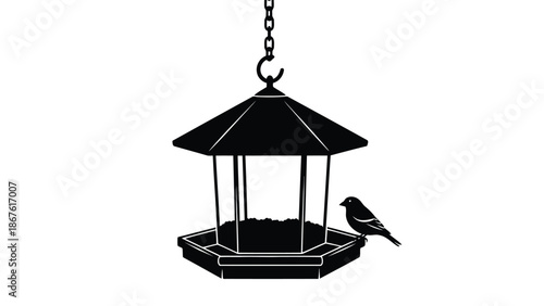 Black silhouette of a bird on a hanging octagonal bird feeder with a pointed roof isolated on white background