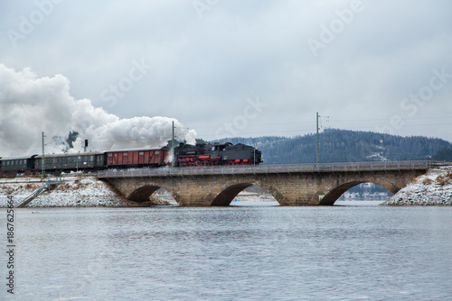 Long steam train crossing bridge in winter countryside