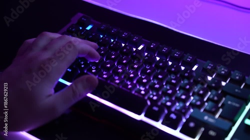 Top side view of man’s hand typing on RGB mechanical keyboard, gaming or programming setup, colorful neon lighting and technology workspace concept