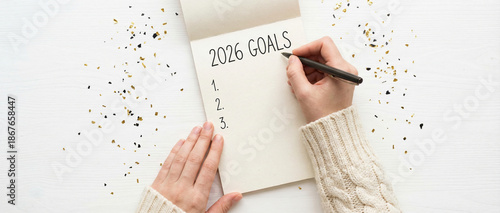 Top overhead above close up flatlay view photo of female hands making noted to the open notebook with inscription 2026 goals