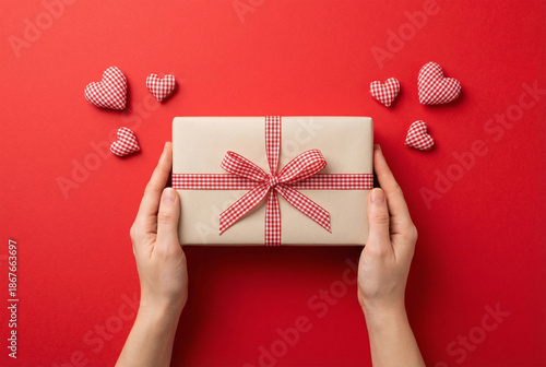 Wallpaper Mural First person top view photo of st valentine's day decorations female hands holding kraft paper giftbox with checkered ribbon bow and hearts on isolated red background Torontodigital.ca