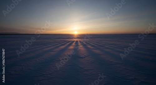 Wide panoramic view of a frozen snowy landscape during a sunrise with long shadows.