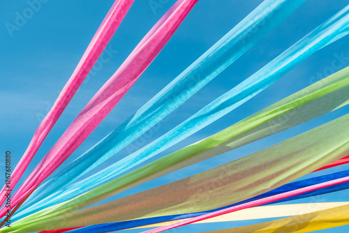 Low angle view of colorful fabric ribbons waving in the wind against blue sky during summer festival celebration