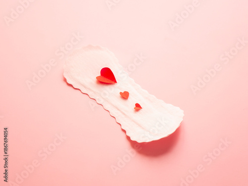 Sanitary pad with red paper hearts on pink background concept of menstruation and feminine hygiene
