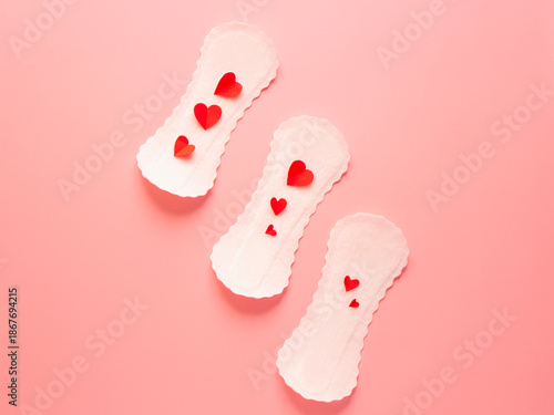 Seamless pattern of white sanitary pads with red paper hearts on pink background menstruation and feminine hygiene concept