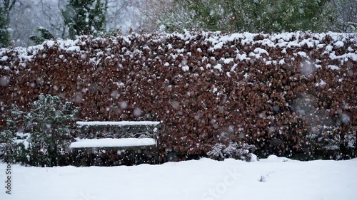 Serene winter garden scene with empty bench and heavy snowfall in slow motion
