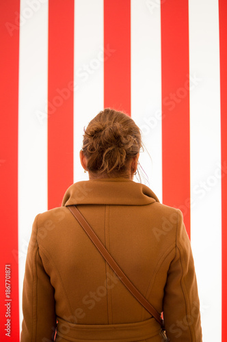 Woman in Camel Coat Looking at Red and White Striped Background