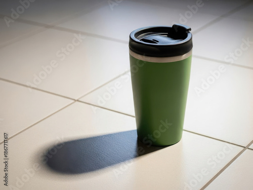 Green travel mug on tiled floor